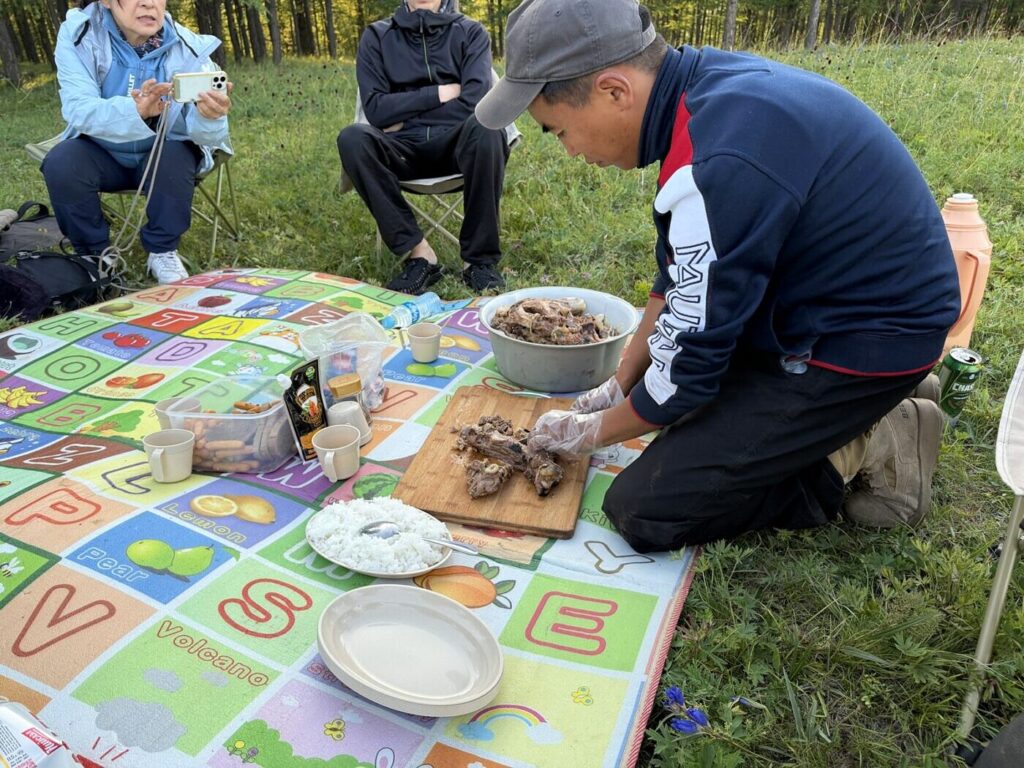 草原のテント泊地でホルホグを切り分けるスタッフ