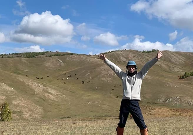 草原と丘で人が両手を広げている写真