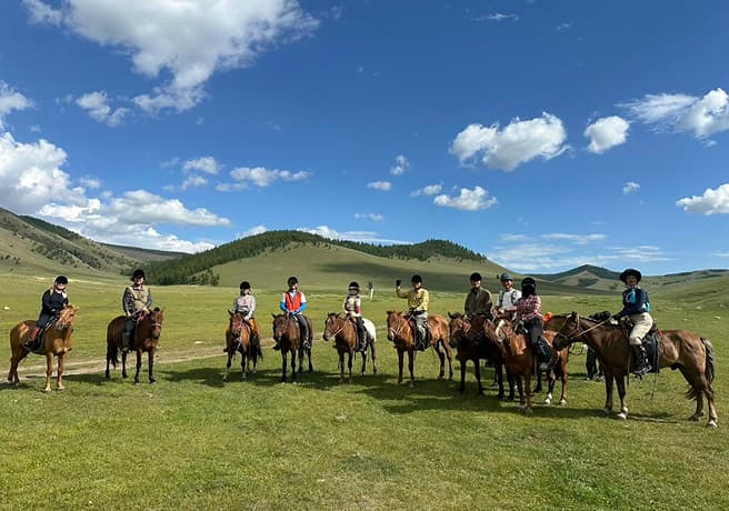 青空と草原で乗馬している写真